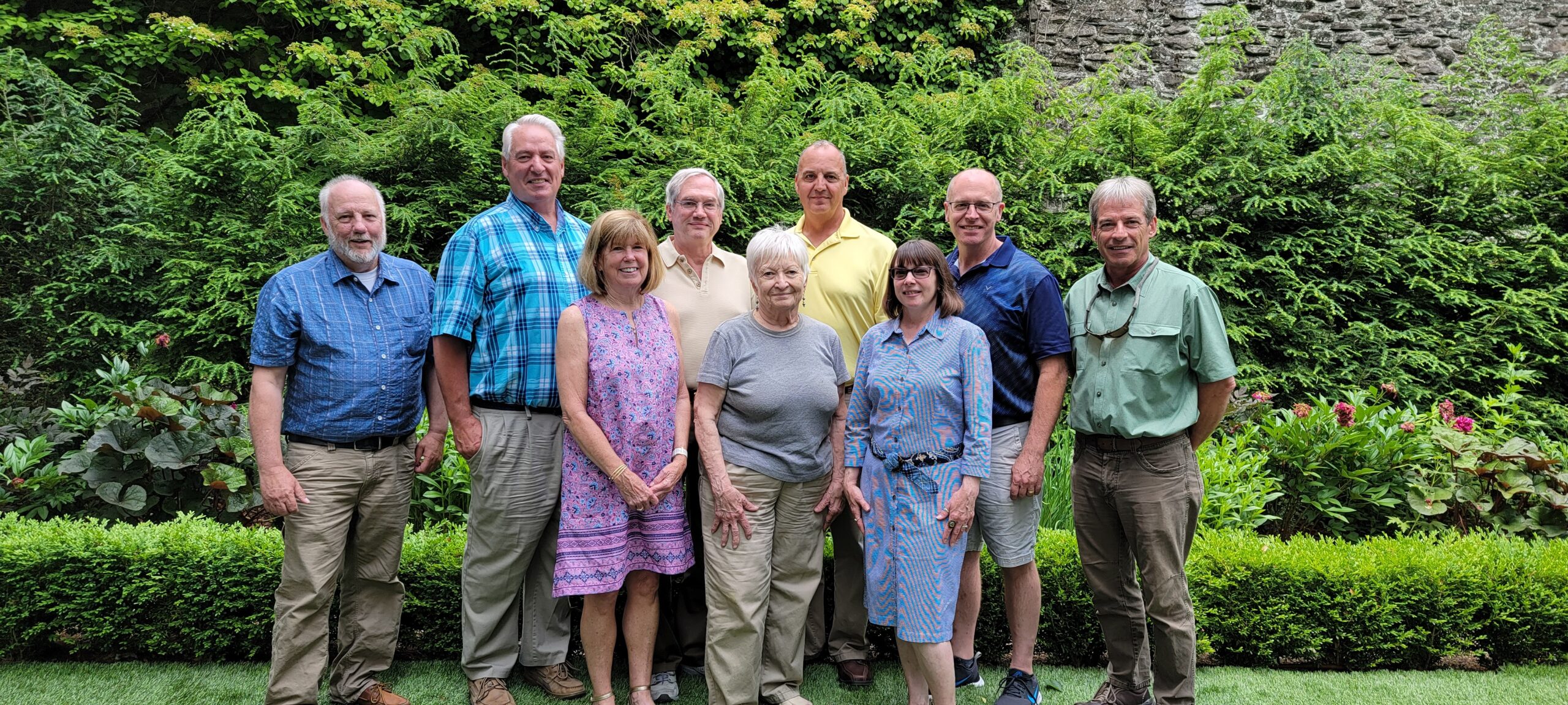 The members of the PCCD Board posing for a group photograph in front of landscaped trees