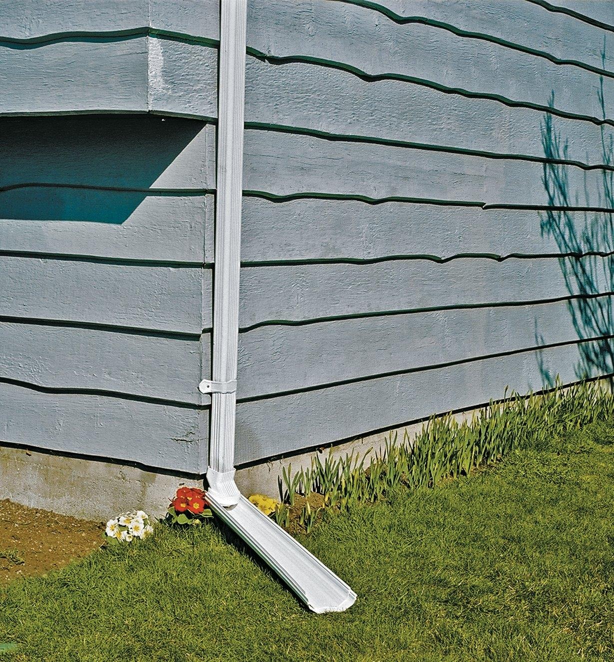 A plastic downspout emptying off of a house and onto a grass lawn