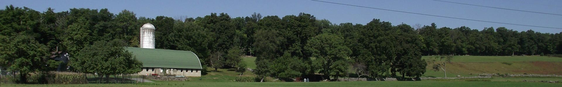 A field with a barn, silo, and trees in the distance