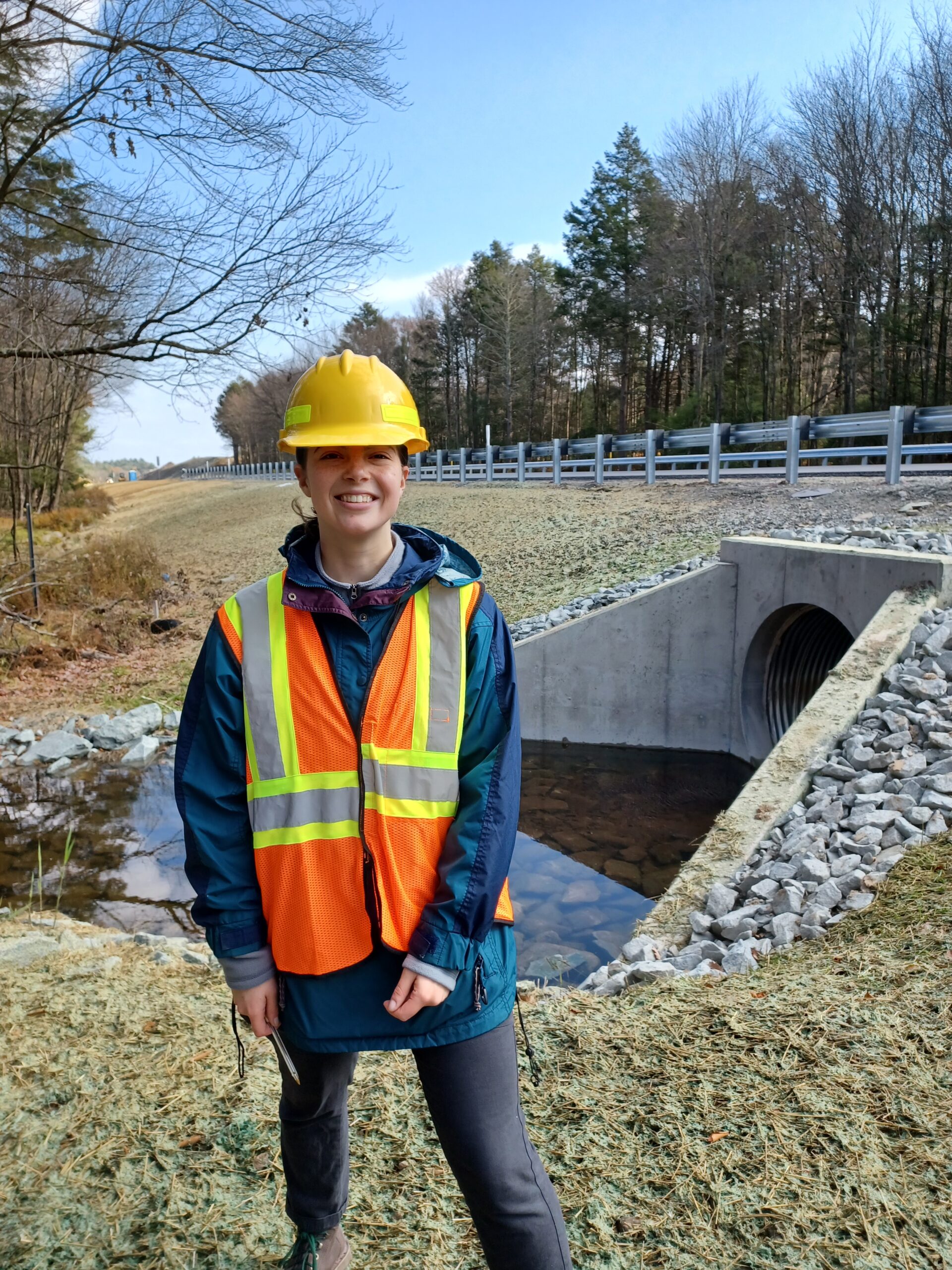 Resource Conservationist Ally poses next to State Route 84 with a hardhat and safety vest