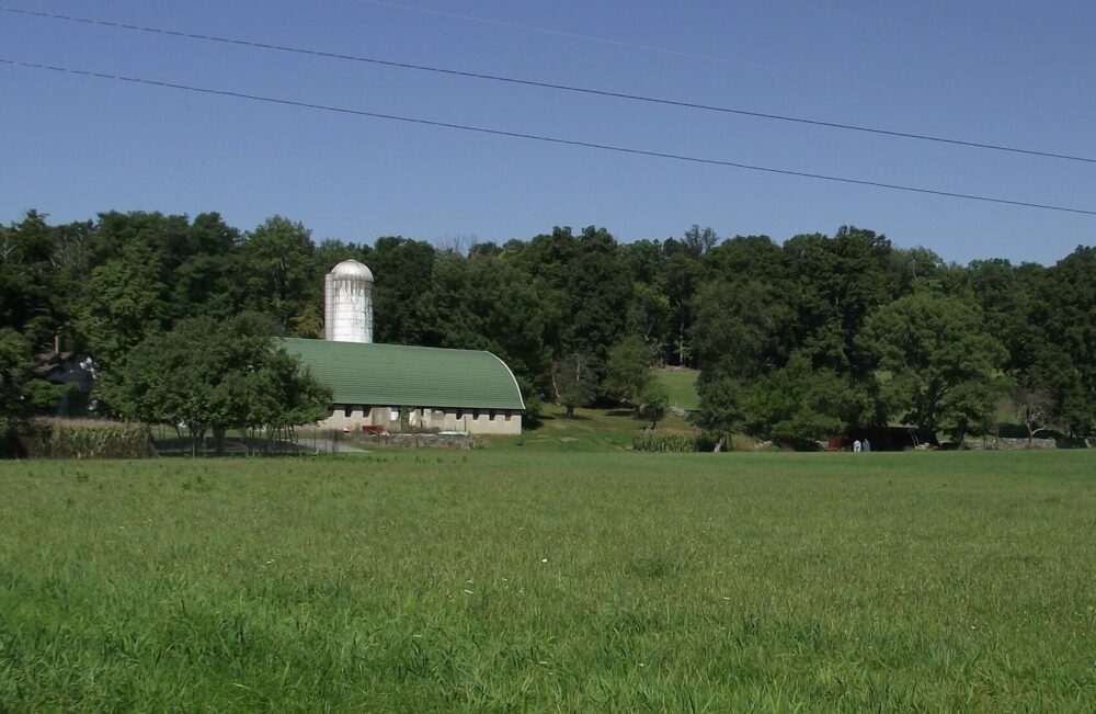 A field with a barn, silo, and trees in the distance