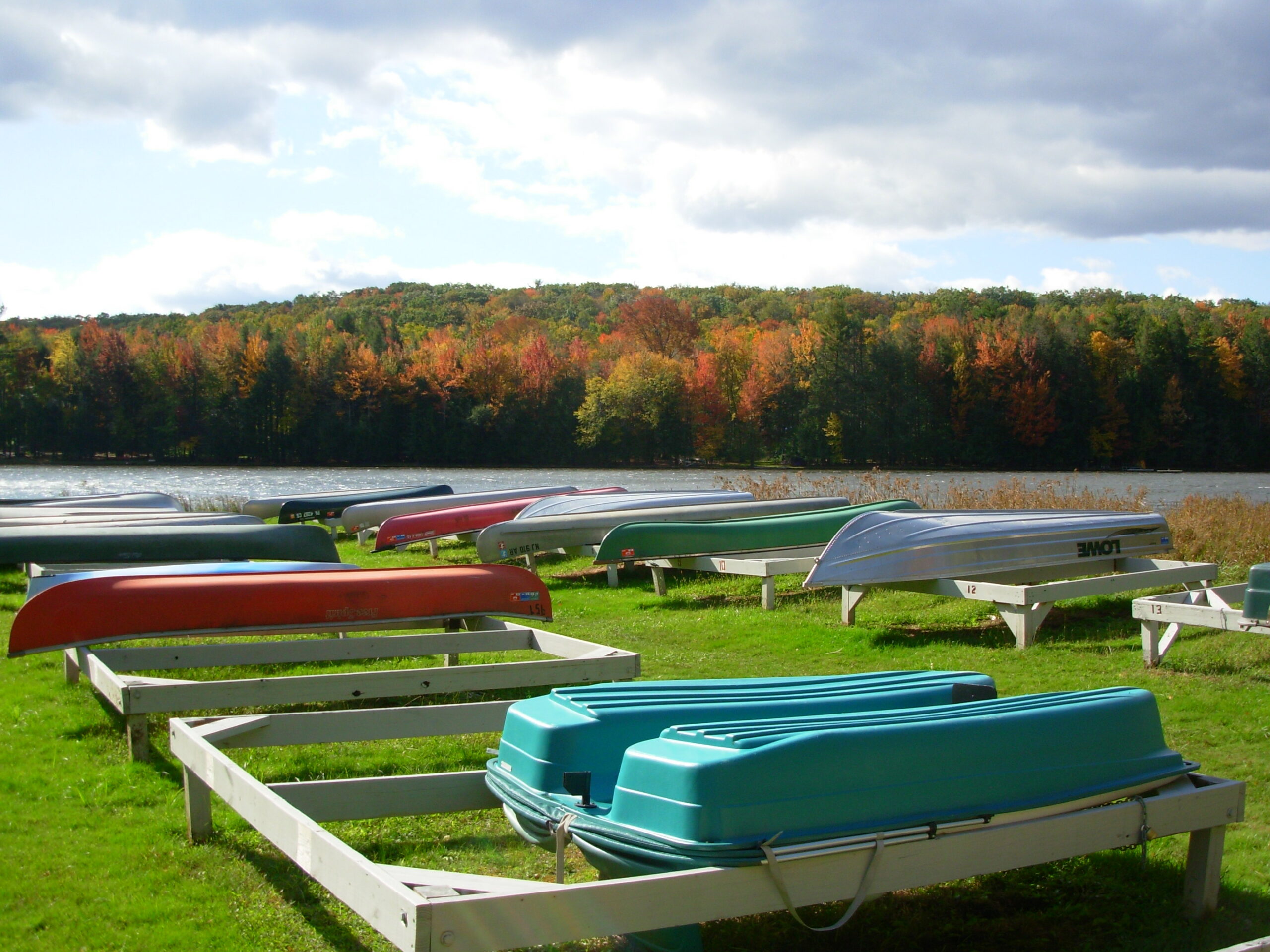Canoes and paddle boats on the shore of a lake with fall foliage in the background