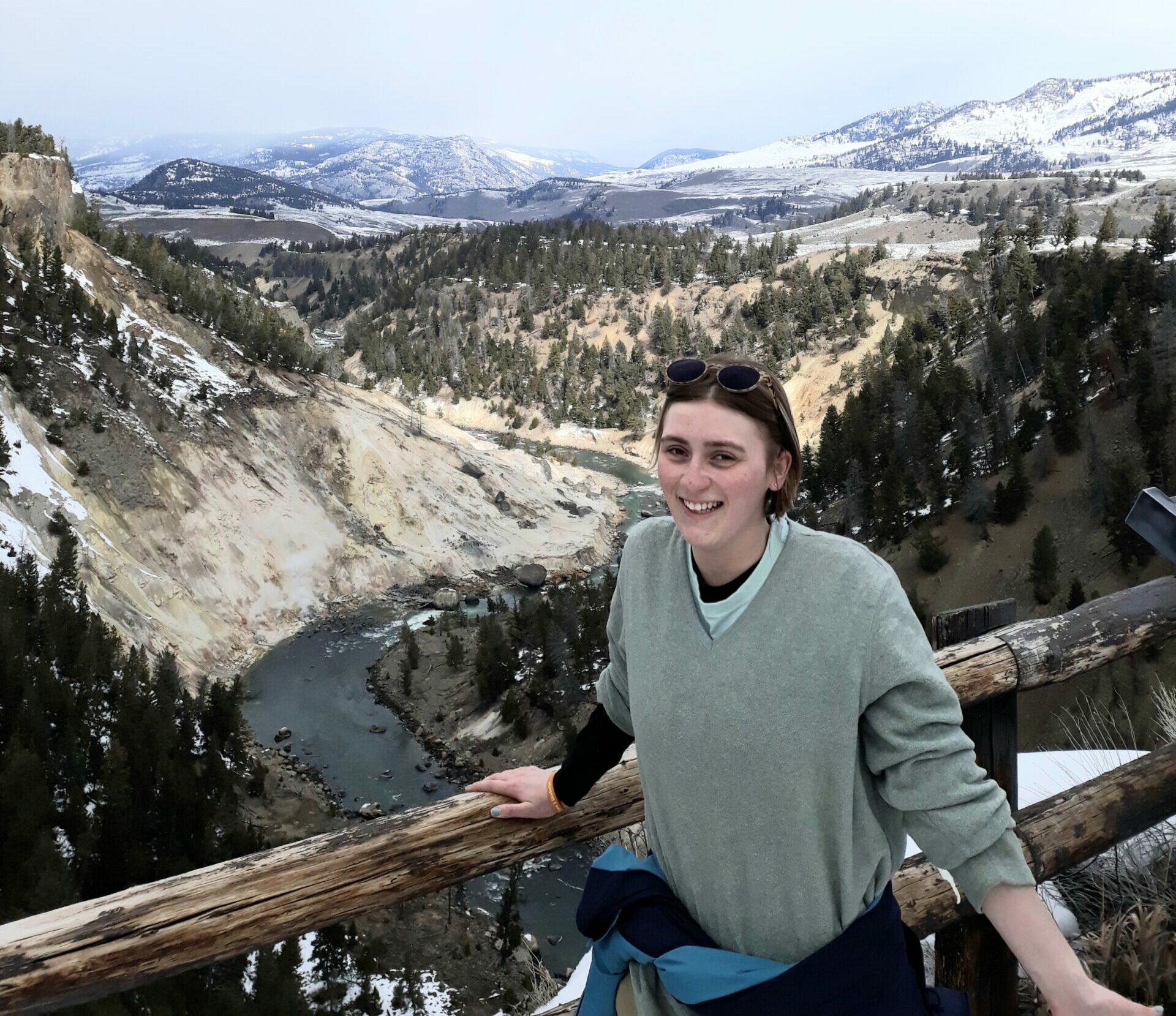 Communications Coordinator Emily stands at a scenic overlook with mountains behind