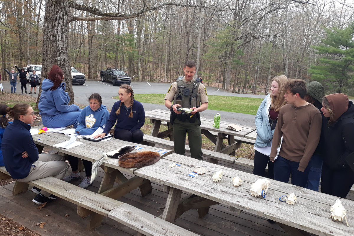 students listening to a game commission officer outside around a table with wildlife skulls