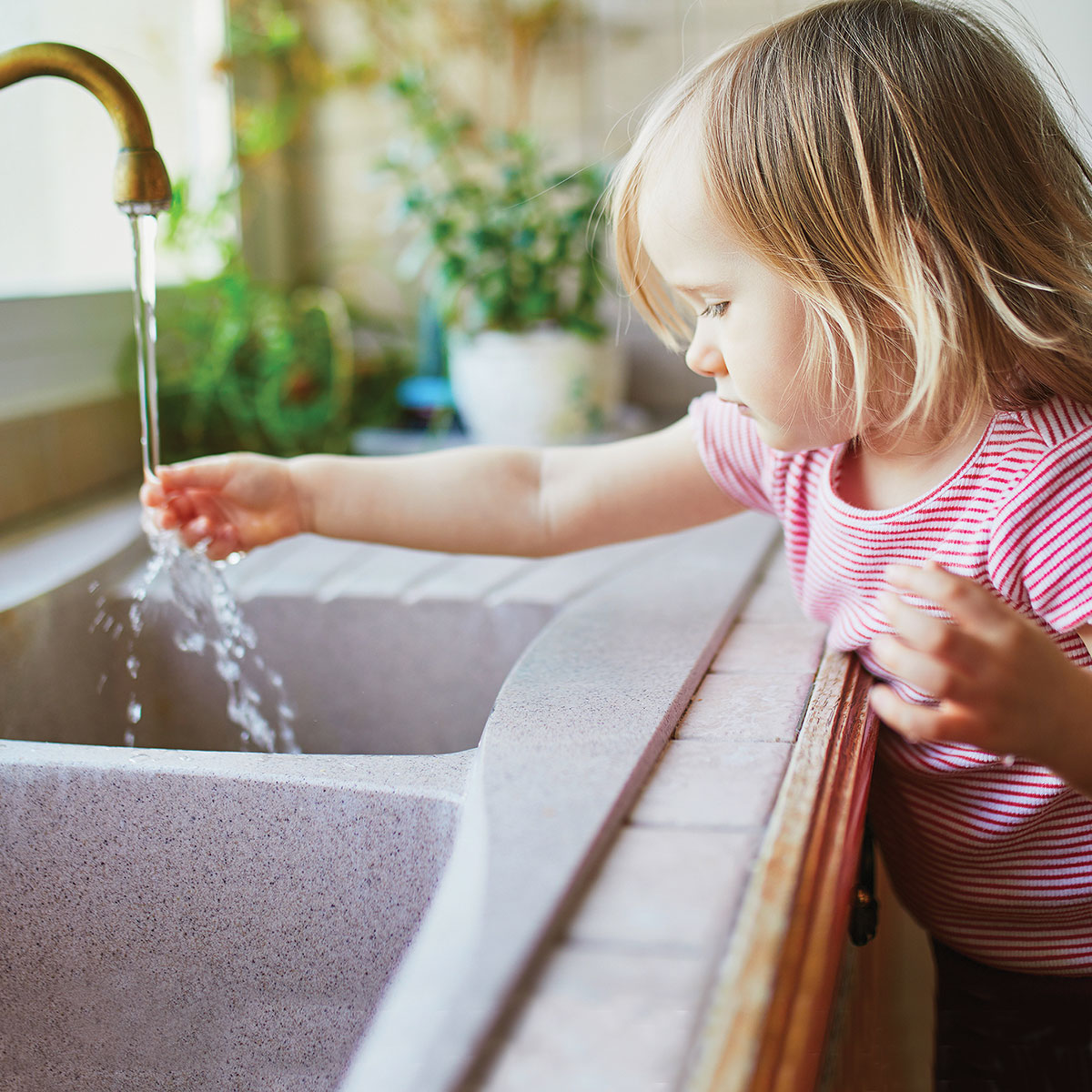 Girl at sink with hand in running faucet