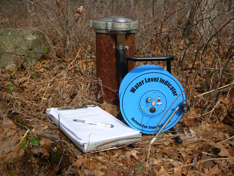 A wellhead with a clipboard next to it and a water level indicator