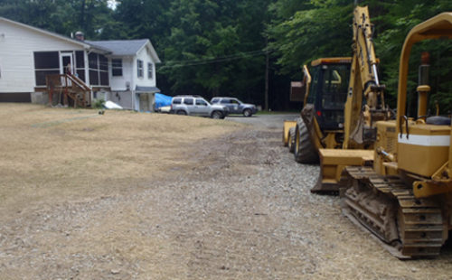 Two construction vehicles parked on a clearing next to a house