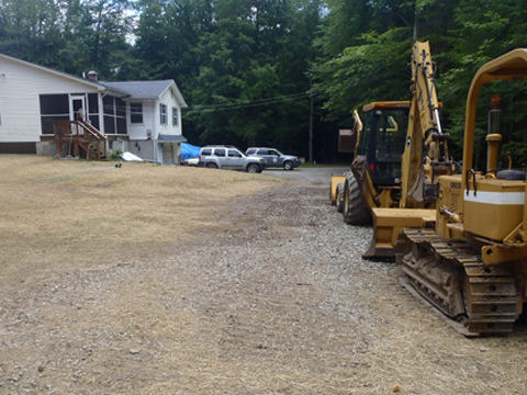 Two construction vehicles parked on a clearing next to a house