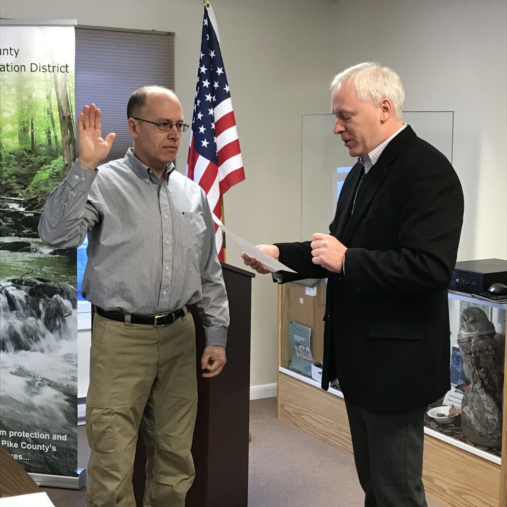 Two men, one raising his hand and the other reading from a sheet of paper