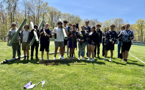 Students pose in a group with tree sleeves while planting trees on campus