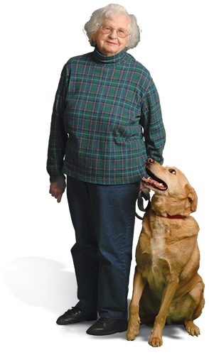 A woman standing and looking at the camera with a large dog at her side