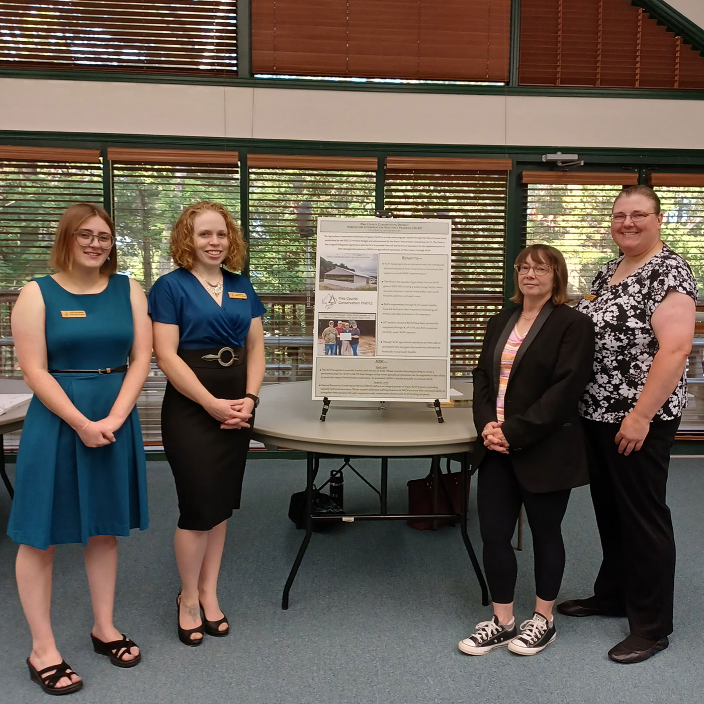 Four people posing for a group photo next to a tabletop poster