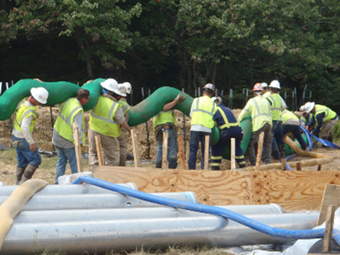 A construction site with a group of people holding up a silt sock