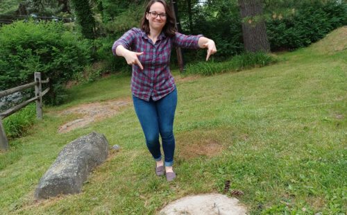 Watershed Specialist Rachael by the District's septic system cap and enthusiastically points to it