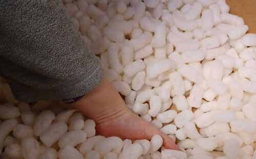 A hand reaching into a cardboard box of biodegradable packing peanuts