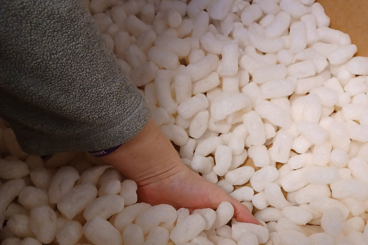 A hand reaching into a cardboard box of biodegradable packing peanuts