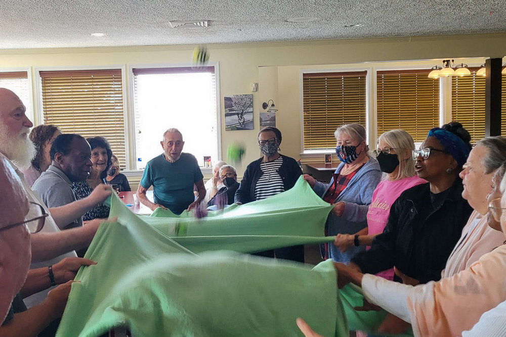 A group of senior citizens hold onto the edges of three green blankets and bounce stuffed bumble bees between them