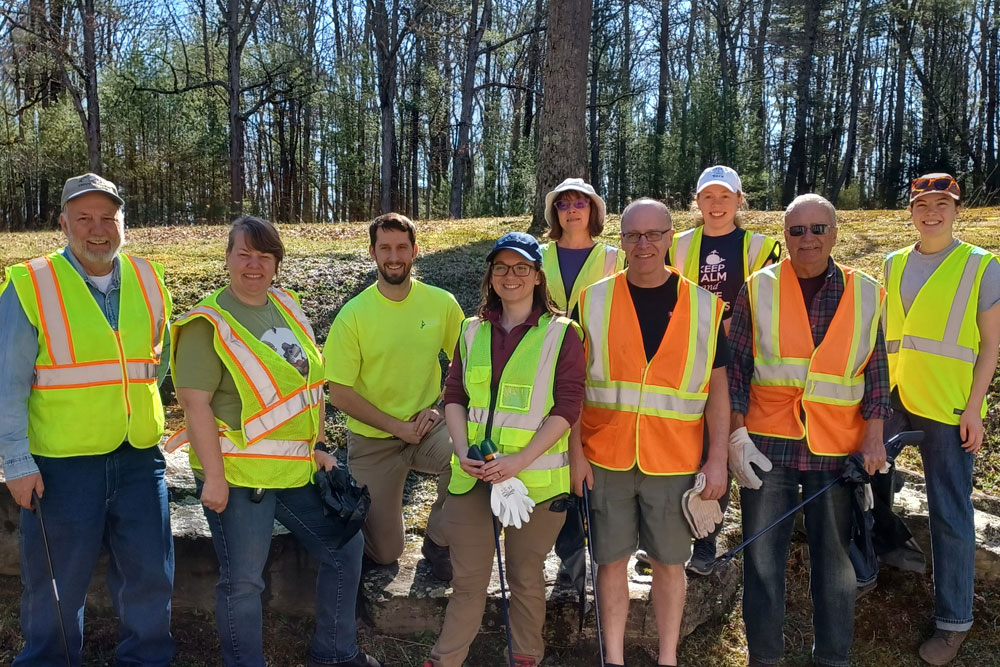 A group of PCCD staff, board members, and partners pose for a photo in safety vests after the semi-annual road cleanup