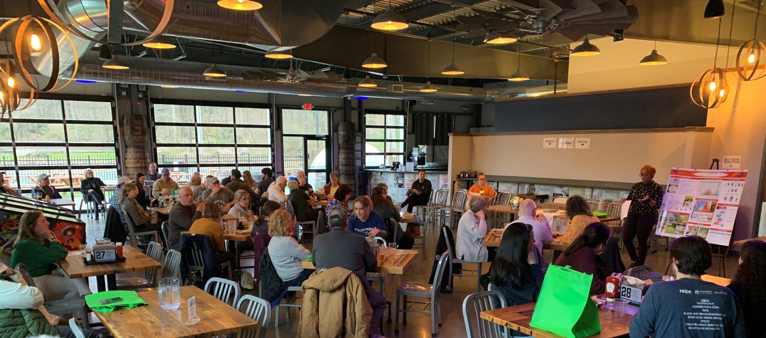 A large group of people seated in a restaurant listening to a speaker at the front of the room