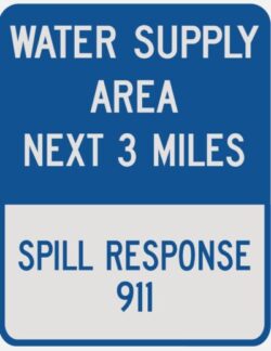 Example of a blue and white spill response sign found along roadways with the text "water supply area next three miles, spill response 911"