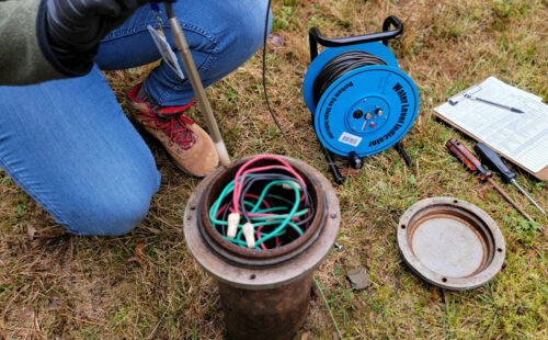 Close up of a private well in a grassy area and the tools our Watershed Specialist uses to measure the depth to the water table