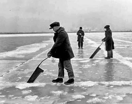 A black and white photo of three people standing on a frozen lake cutting through the ice with saws