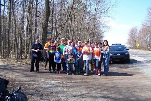 A group of people pose together for a photo at a wooded area on the side of the road