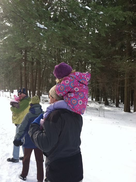 A group of adults and kids walking through a snowy woods