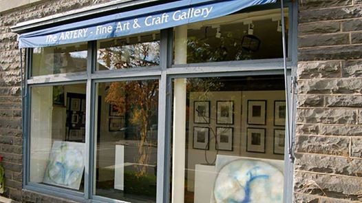 Storefront window with framed artwork visible inside and an awning outside with the words "The Artery- Fine Art & Craft Gallery"