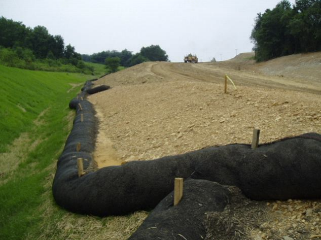 A compost filter sock at the bottom of a slope near a roadway under construction