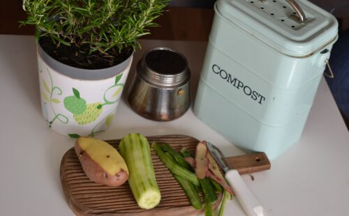 A tabletop compost jar and a cutting board with food scraps