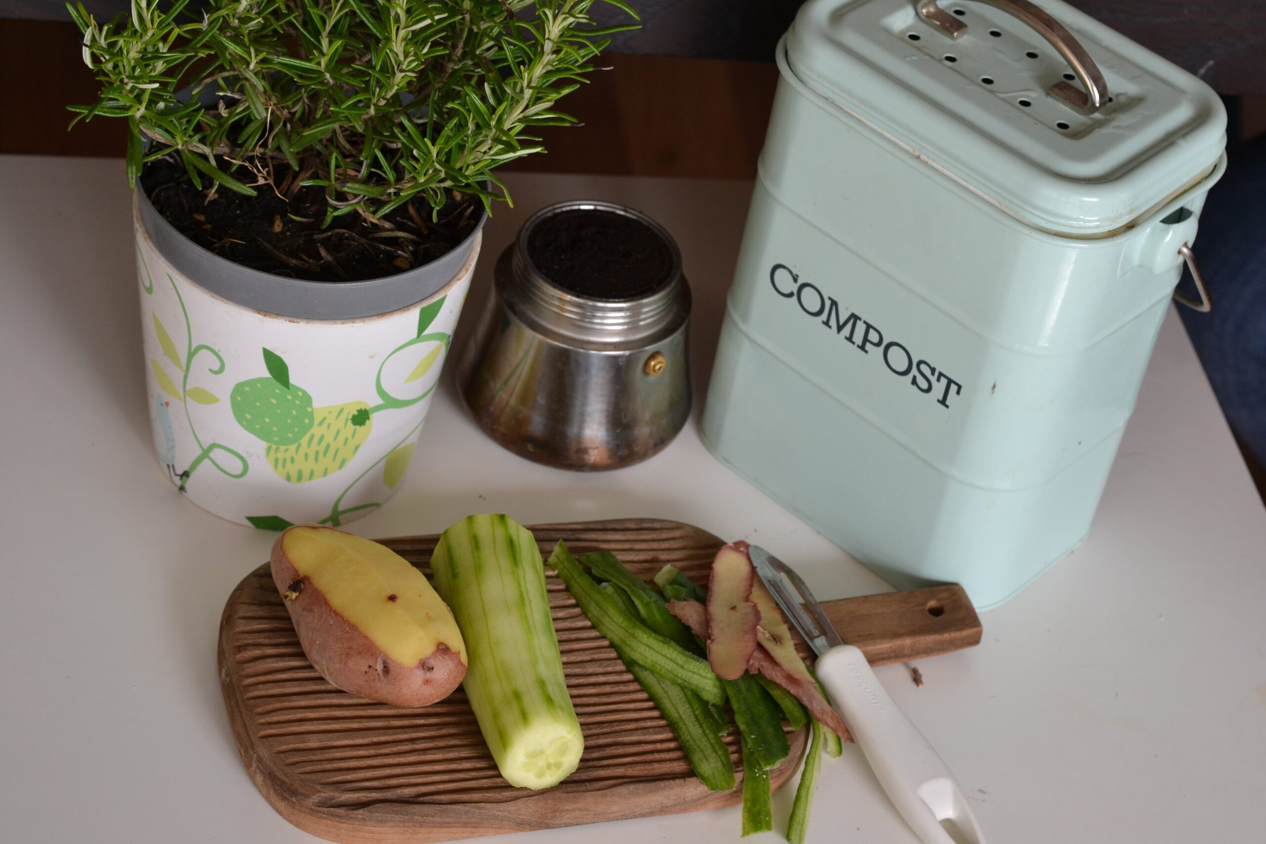 A tabletop compost jar and a cutting board with food scraps