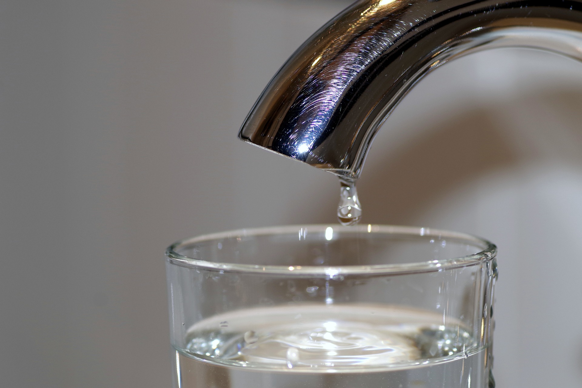 A faucet drips into a drinking glass