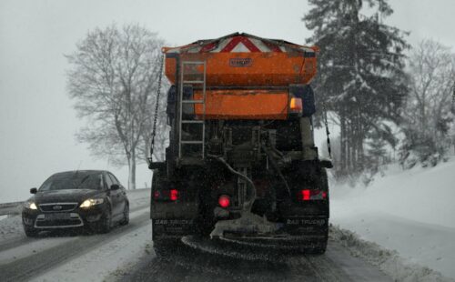 A truck goes down a snowy road with a large brush